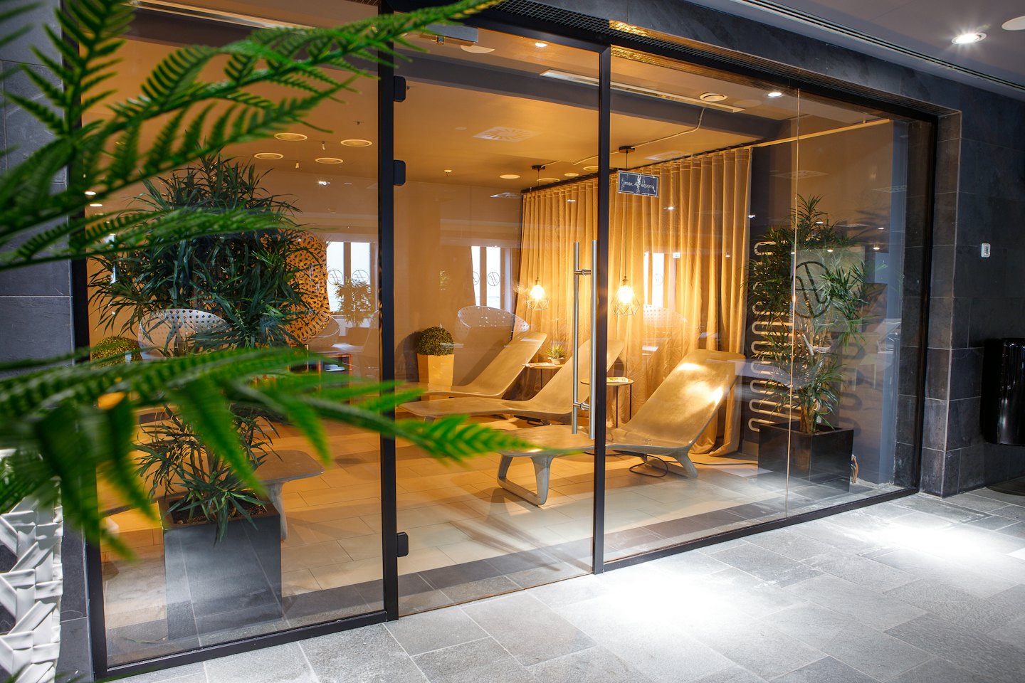 Moderner Spa-Ruheraum mit grauen Liegestühlen und grünen Pflanzen.